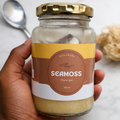 Jar of Seamoss Pure Gel held by a hand with a spoon and sponge in the background.